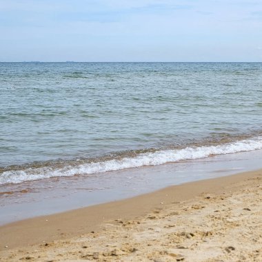 Sakin ve sakin bir denizin sakin bir yatay görüntüsü. Yumuşak dalgalar kumlu bir kumsalın kıyısına vuruyor. Kompozisyon basit ve dengeli. Boşluğu kopyala