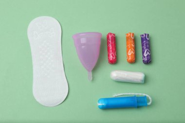 Kadınsı pedler, tamponlar, regl kupası yeşil arka planda dişi hijyen ürünleri