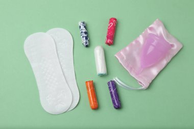 Kadınsı pedler, tamponlar, regl kupası yeşil arka planda dişi hijyen ürünleri