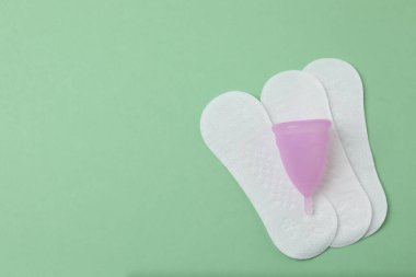 Kadınsı pedler, tamponlar, regl kupası yeşil arka planda dişi hijyen ürünleri