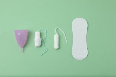Kadınsı pedler, tamponlar, regl kupası yeşil arka planda dişi hijyen ürünleri