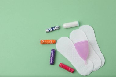 Kadınsı pedler, tamponlar, regl kupası yeşil arka planda dişi hijyen ürünleri