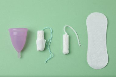 Kadınsı pedler, tamponlar, regl kupası yeşil arka planda dişi hijyen ürünleri