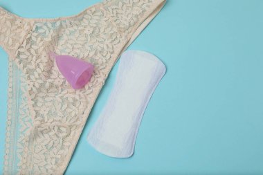 Kadınsı pedler, tamponlar, adet kupası mavi arka planda dişi hijyen ürünleri.