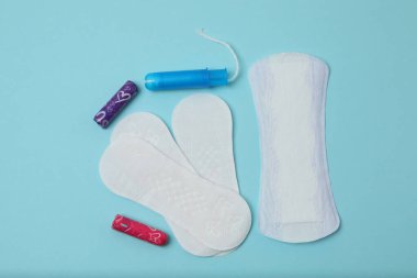 Kadınsı pedler, tamponlar, adet kupası mavi arka planda dişi hijyen ürünleri.