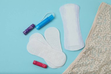 Kadınsı pedler, tamponlar, adet kupası mavi arka planda dişi hijyen ürünleri.