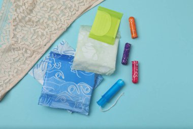 Kadınsı pedler, tamponlar, adet kupası mavi arka planda dişi hijyen ürünleri.