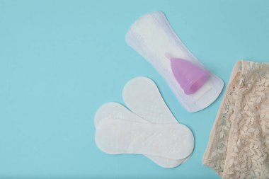 Kadınsı pedler, tamponlar, adet kupası mavi arka planda dişi hijyen ürünleri.