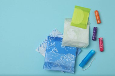 Kadınsı pedler, tamponlar, adet kupası mavi arka planda dişi hijyen ürünleri.