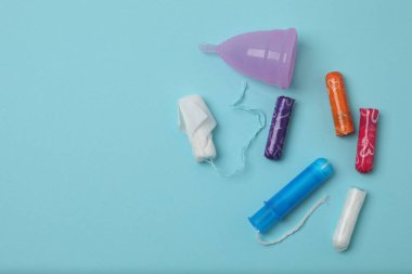 Kadınsı pedler, tamponlar, adet kupası mavi arka planda dişi hijyen ürünleri.