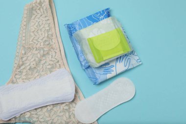 Kadınsı pedler, tamponlar, adet kupası mavi arka planda dişi hijyen ürünleri.
