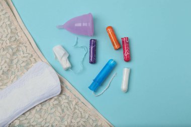Kadınsı pedler, tamponlar, adet kupası mavi arka planda dişi hijyen ürünleri.
