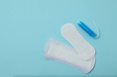 Kadınsı pedler, tamponlar, adet kupası mavi arka planda dişi hijyen ürünleri.