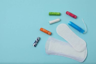 Kadınsı pedler, tamponlar, adet kupası mavi arka planda dişi hijyen ürünleri.