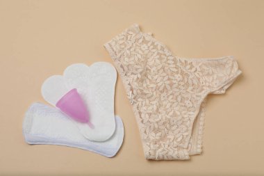 Kadın pedleri, tamponlar, regl kupası bej arka planda kadın hijyen ürünleri.