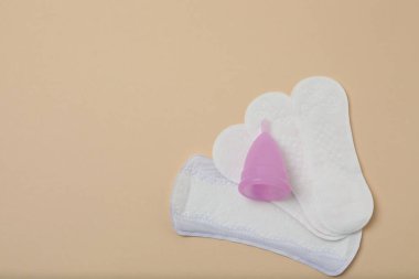 Kadın pedleri, tamponlar, regl kupası bej arka planda kadın hijyen ürünleri.