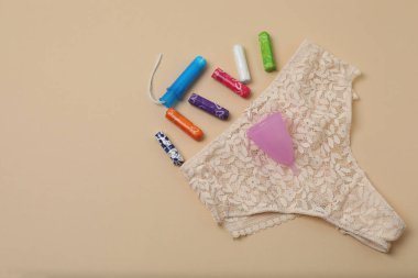 Kadın pedleri, tamponlar, regl kupası bej arka planda kadın hijyen ürünleri.