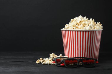 Lezzetli, yumuşak patlamış mısırla dolu, siyah arka planda 3 boyutlu gözlüklü klasik kırmızı ve beyaz çizgili kutu..