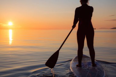 Maceracı bir kürek gemide paddeling bir parlak ve canlı gün batımı sırasında kızdır. Alınan İspanyolca bankalar, Vancouver, British Columbia, Kanada.