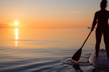 Maceracı bir kürek gemide paddeling bir parlak ve canlı gün batımı sırasında kızdır. Alınan İspanyolca bankalar, Vancouver, British Columbia, Kanada.