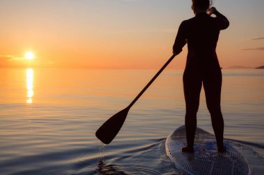 Maceracı bir kürek gemide paddeling bir parlak ve canlı gün batımı sırasında kızdır. Alınan İspanyolca bankalar, Vancouver, British Columbia, Kanada.