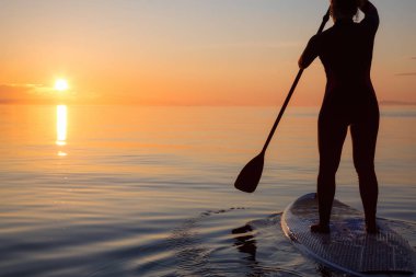 Maceracı bir kürek gemide paddeling bir parlak ve canlı gün batımı sırasında kızdır. Alınan İspanyolca bankalar, Vancouver, British Columbia, Kanada.
