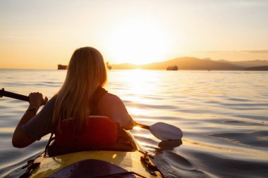Bir kayık üzerinde canlı bir gün batımı sırasında paddeling okyanusta kadındır. Vancouver, British Columbia, Kanada çekilmiş. Konsept: macera, tatil, yaşam tarzı, spor, eğlence, etkinlik, tatil