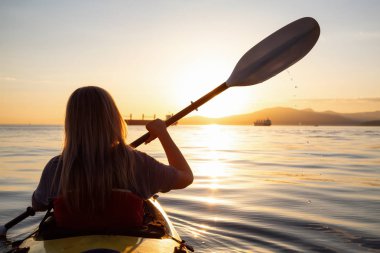 Bir kayık üzerinde canlı bir gün batımı sırasında paddeling okyanusta kadındır. Vancouver, British Columbia, Kanada çekilmiş. Konsept: macera, tatil, yaşam tarzı, spor, eğlence, etkinlik, tatil