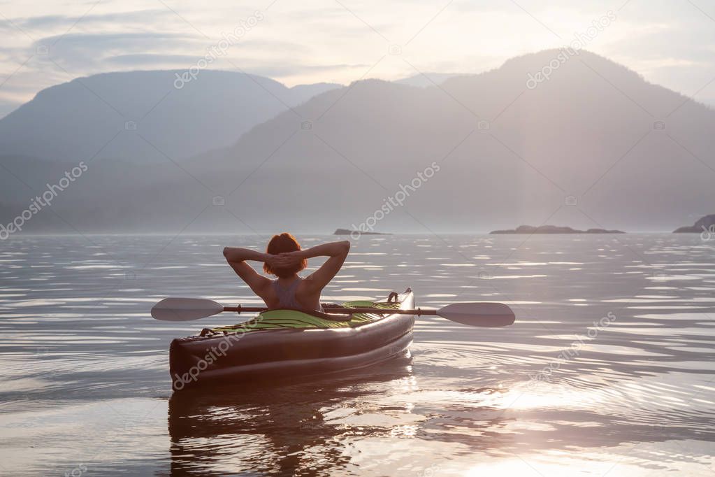 Woman on a kayak is enjoying the beautiful Canadian Mountain Landscape during a vibrant sunset. Taken in Howe Sound, North of Vancouver, British Columbia, Canada.