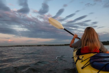 Bir kayık üzerinde canlı bir gün batımı sırasında paddeling okyanusta kadındır. Vancouver, British Columbia, Kanada çekilmiş. Konsept: macera, tatil, yaşam tarzı, spor, eğlence, etkinlik, tatil