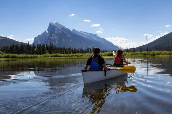 Couple adventurous friends are canoeing in a lake surrounded by the Canadian Mountains. Taken in Vermilion Lakes, Banff, Alberta, Canada.