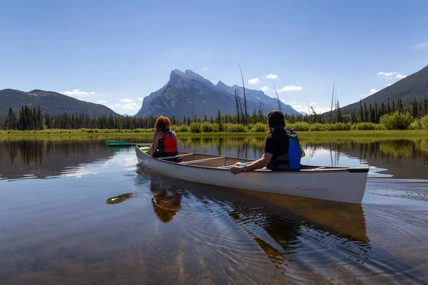 Couple adventurous friends are canoeing in a lake surrounded by the Canadian Mountains. Taken in Vermilion Lakes, Banff, Alberta, Canada.