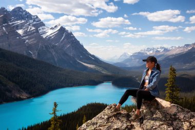 Kanada Kayalık Dağları ve Peyto göl güzel bakan sarp bir kayalığın kenarında oturan maceracı kız. Banff National Park, Alberta, Kanada içinde alınan.