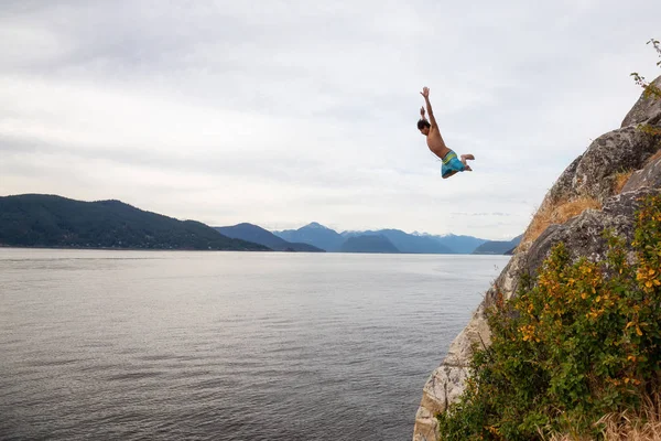 Adventurous man is cliff jumping from a rock into the ocean. Taken in Whytecliff Park, Horseshoe Bay, West Vancouver, BC, Canada.