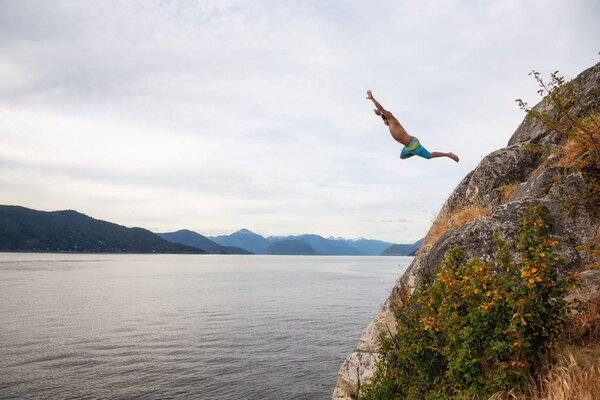 Adventurous man is cliff jumping from a rock into the ocean. Taken in Whytecliff Park, Horseshoe Bay, West Vancouver, BC, Canada.