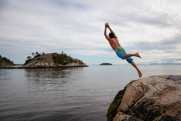 Adventurous man is cliff jumping from a rock into the ocean. Taken in Whytecliff Park, Horseshoe Bay, West Vancouver, BC, Canada.