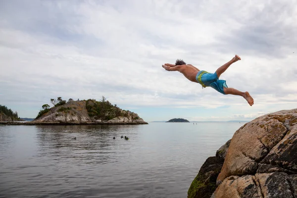 Adventurous man is cliff jumping from a rock into the ocean. Taken in Whytecliff Park, Horseshoe Bay, West Vancouver, BC, Canada.