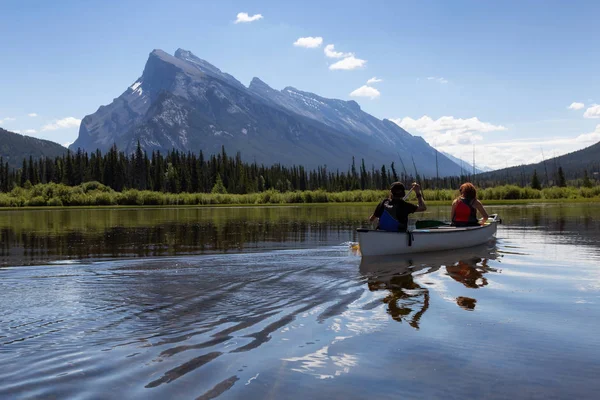 Couple adventurous friends are canoeing in a lake surrounded by the Canadian Mountains. Taken in Vermilion Lakes, Banff, Alberta, Canada.