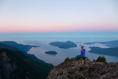 Bir dağ uçurumun tepesinde maceracı kadın güzel yaz güneşin tadını çıkarıyor. Mount Brunswick, aslanlar Bay, Vancouver, Bc, Kanada kuzeyindeki üzerinde gerçekleştirilen.