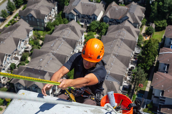 Burnaby, Vancouver, British Columbia, Canada - July 05, 2018: High rise rope access window cleaner is working during a hot sunny summer day.