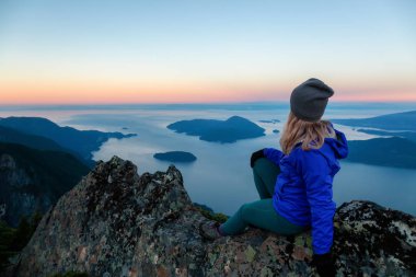 Bir dağ uçurumun tepesinde maceracı kadın güzel yaz güneşin tadını çıkarıyor. Mount Brunswick, aslanlar Bay, Vancouver, Bc, Kanada kuzeyindeki üzerinde gerçekleştirilen.