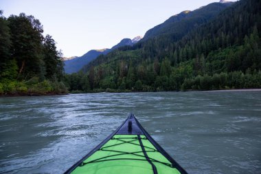 Bir canlı yaz gün batımı sırasında Kanada dağlarla çevrili bir nehir kanosu. Squamish, British Columbia, Kanada alınan.