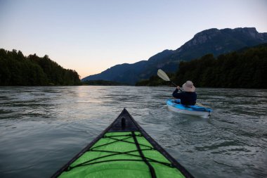 Bir canlı yaz gün batımı sırasında Kanada dağlarla çevrili bir nehir kanosu. Squamish, British Columbia, Kanada alınan.