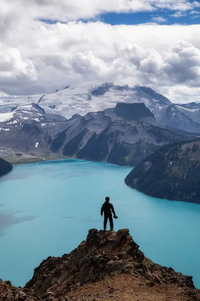 Man standing on top of the Mountain overlooking a beautiful glacier lake. Taken on Panorama Ridge, Garibaldi, Near Whister, BC, Canada.