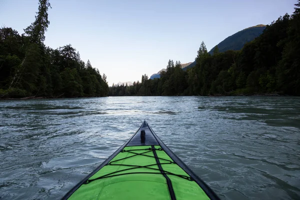 Kayaking in a river surrounded by Canadian Mountains during a vibrant summer sunset. Taken in Squamish, British Columbia, Canada.