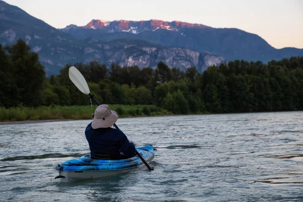 Kayaking in a river surrounded by Canadian Mountains during a vibrant summer sunset. Taken in Squamish, British Columbia, Canada.