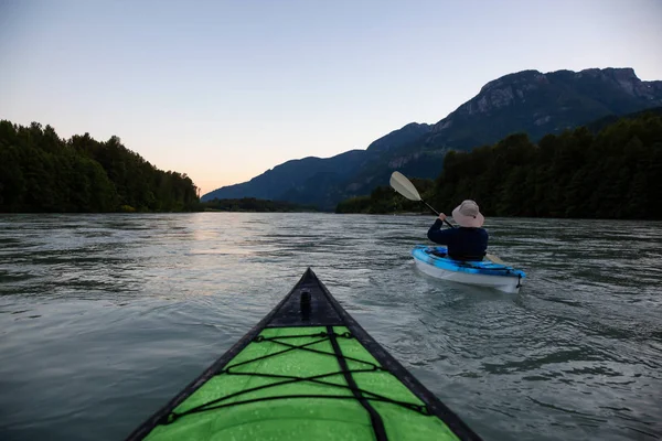 Kayaking in a river surrounded by Canadian Mountains during a vibrant summer sunset. Taken in Squamish, British Columbia, Canada.