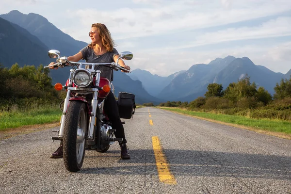 Woman riding a motorcycle on a scenic road surrounded by Canadian Mountains. Taken in Pitt Meadows, Greater Vancouver, BC, Canada.