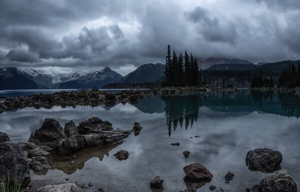 Beautiful landscape view of a Glacier Lake during a dark and moody cloudy sunset. Taken in Garibaldi Provincial Park, located near Whister and Squamish, North of Vancouver, BC, Canada.