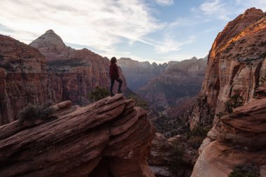 Bir uçurumun kenarında, maceracı kız güzel manzaralı Kanyon canlı bir gün batımı sırasında bakıyor. Zion National Park, Utah, Amerika Birleşik Devletleri'nde çekilen.